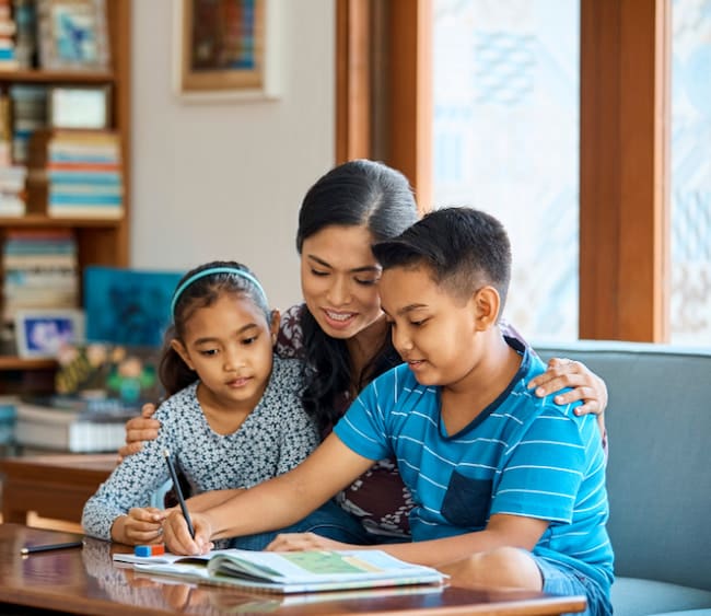 A mom sits down with her two small children at the dinner table to work on homework